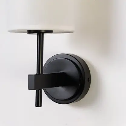 Closeup of black metal wall light with tall white fabric shade showing premium detailing for modern indoor lighting in stylish home interiors.
