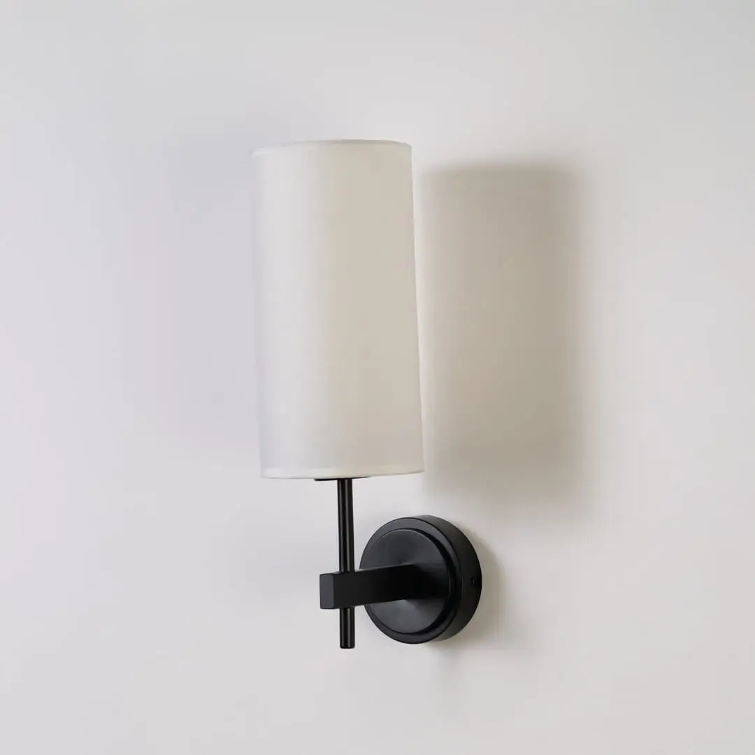 Black metal wall light with tall white fabric shade shown on a clean white background with light off highlighting its sleek modern design.