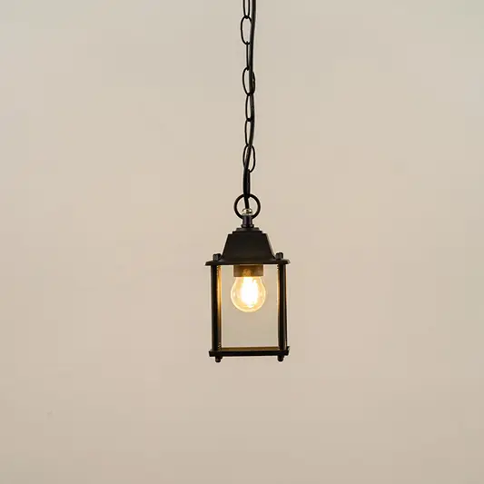 Black metal hanging outdoor lantern with square glass enclosure glowing on white background suitable for porch entrance and exterior decor lighting.