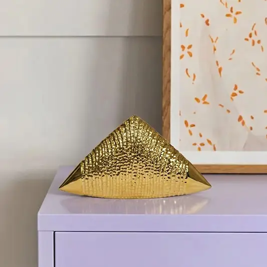 Gold metal pyramid decor accent placed on console table for luxury modern home decor styling ideas.