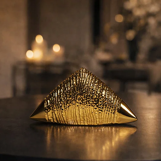 Gold striped ceramic triangle decor placed on table with warm lighting adding luxurious and modern touch to living space.