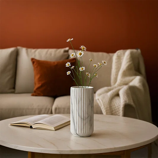 A marble textured cylindrical vase styled against a warm terracotta backdrop creating a modern refined look with soft grey veining details.