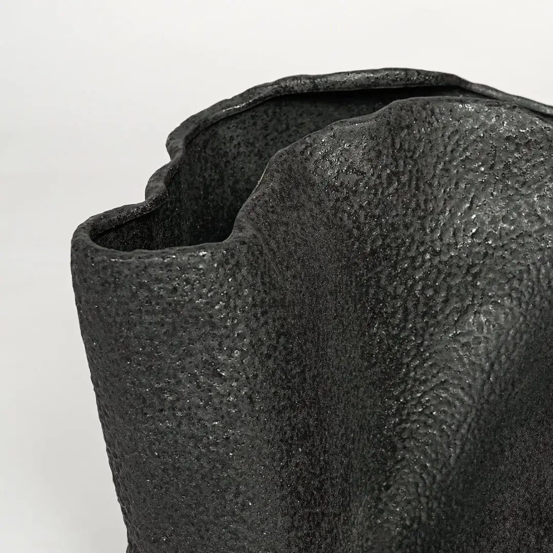 Detailed closeup of black metal decorative vase showcasing rough textured surface and abstract form.