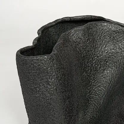 Detailed closeup of black metal decorative vase showcasing rough textured surface and abstract form.
