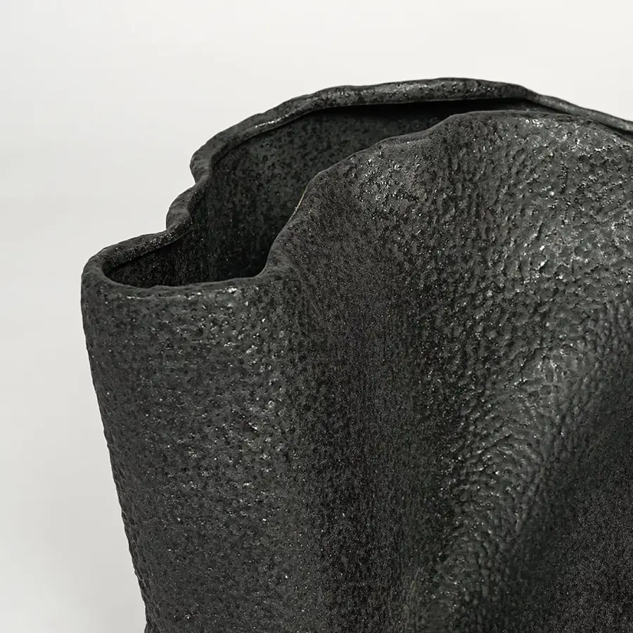 Detailed closeup of black metal decorative vase showcasing rough textured surface and abstract form.
