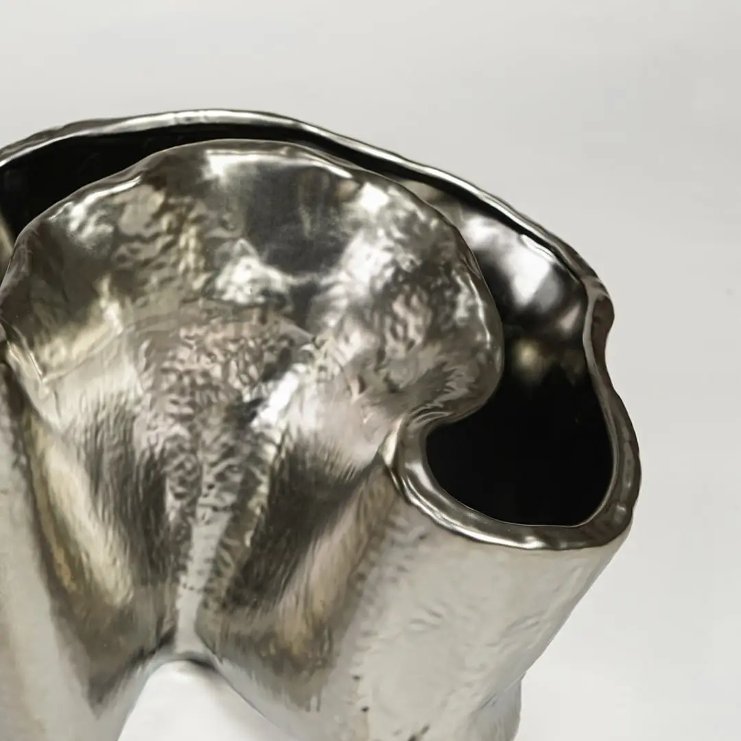 Close view of silver metal decorative vase featuring organic sculpted form and reflective polished finish.