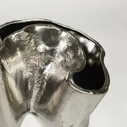 Close view of silver metal decorative vase featuring organic sculpted form and reflective polished finish.