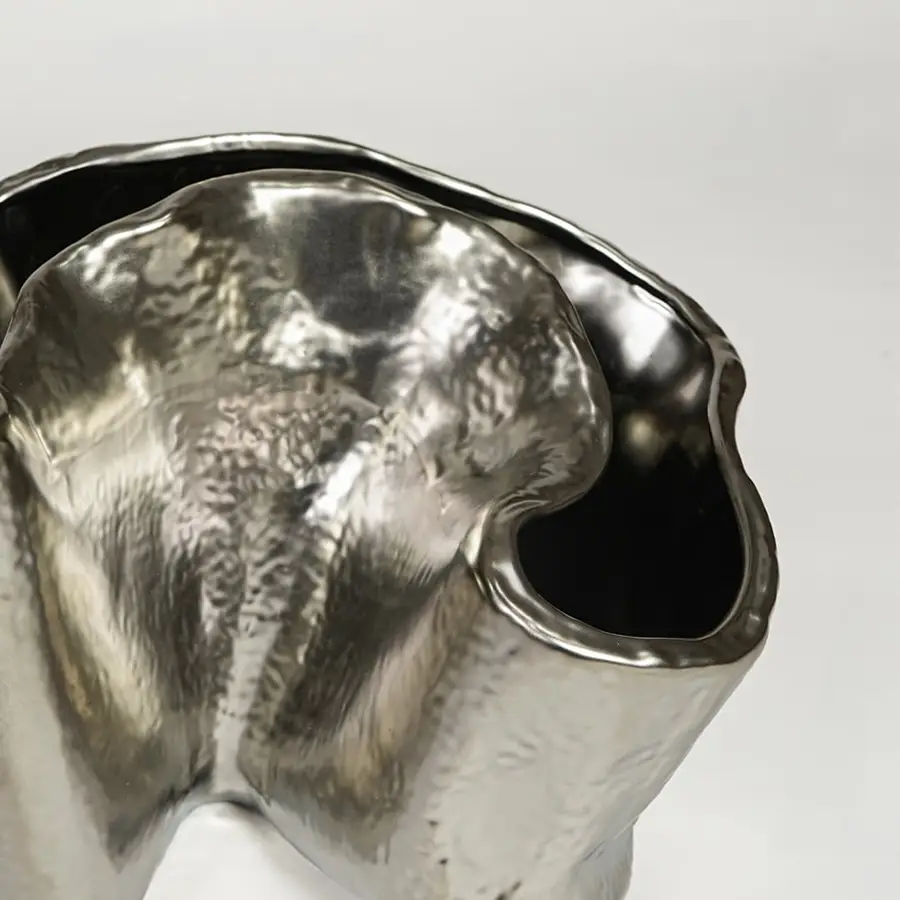 Close view of silver metal decorative vase featuring organic sculpted form and reflective polished finish.