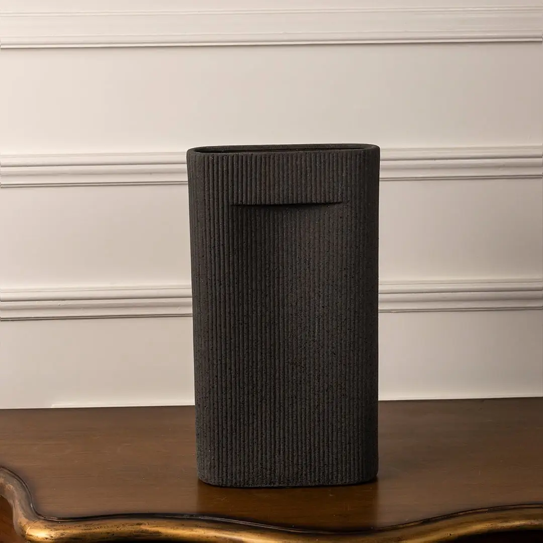 Matte black ribbed vase with sleek rectangular form standing on white background reflecting elegant modern artistry.