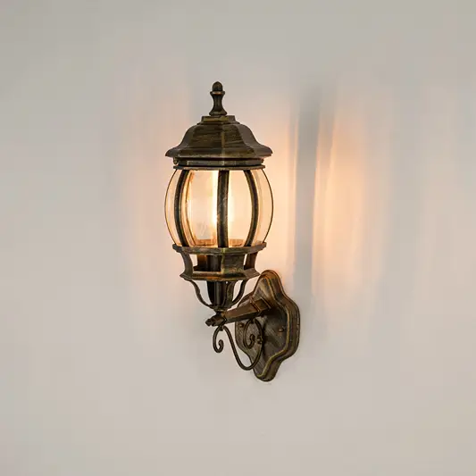 Antique brass outdoor wall sconce on white background with a rounded clear glass cage lantern for entry pathway decor.