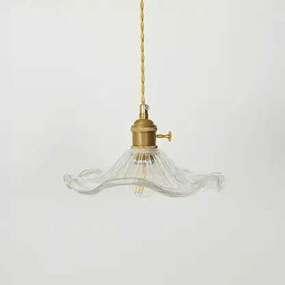 A vintage-style pendant light with a clear ribbed glass shade that has a wavy, flared rim and a brass-colored metal fixture and cord, shown against a plain light gray background.