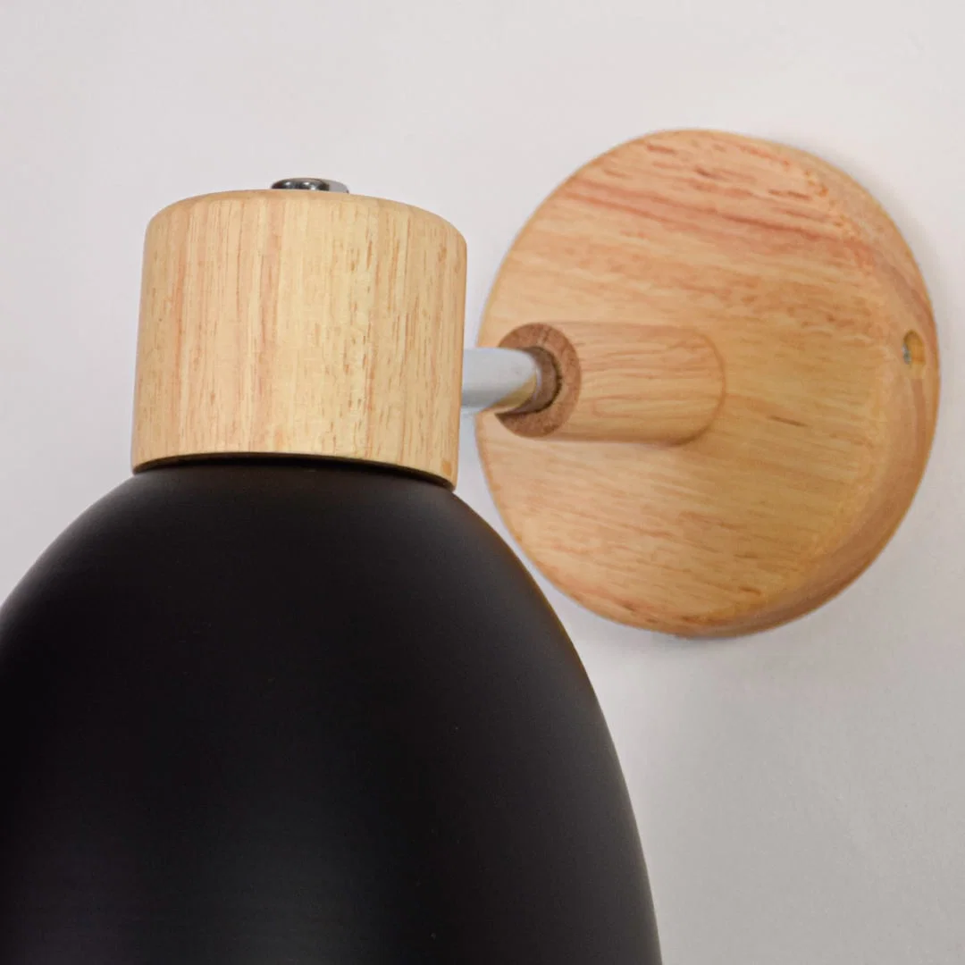 Black metal wall light closeup showing natural wood mount and smooth matte shade finish for modern interior decor.