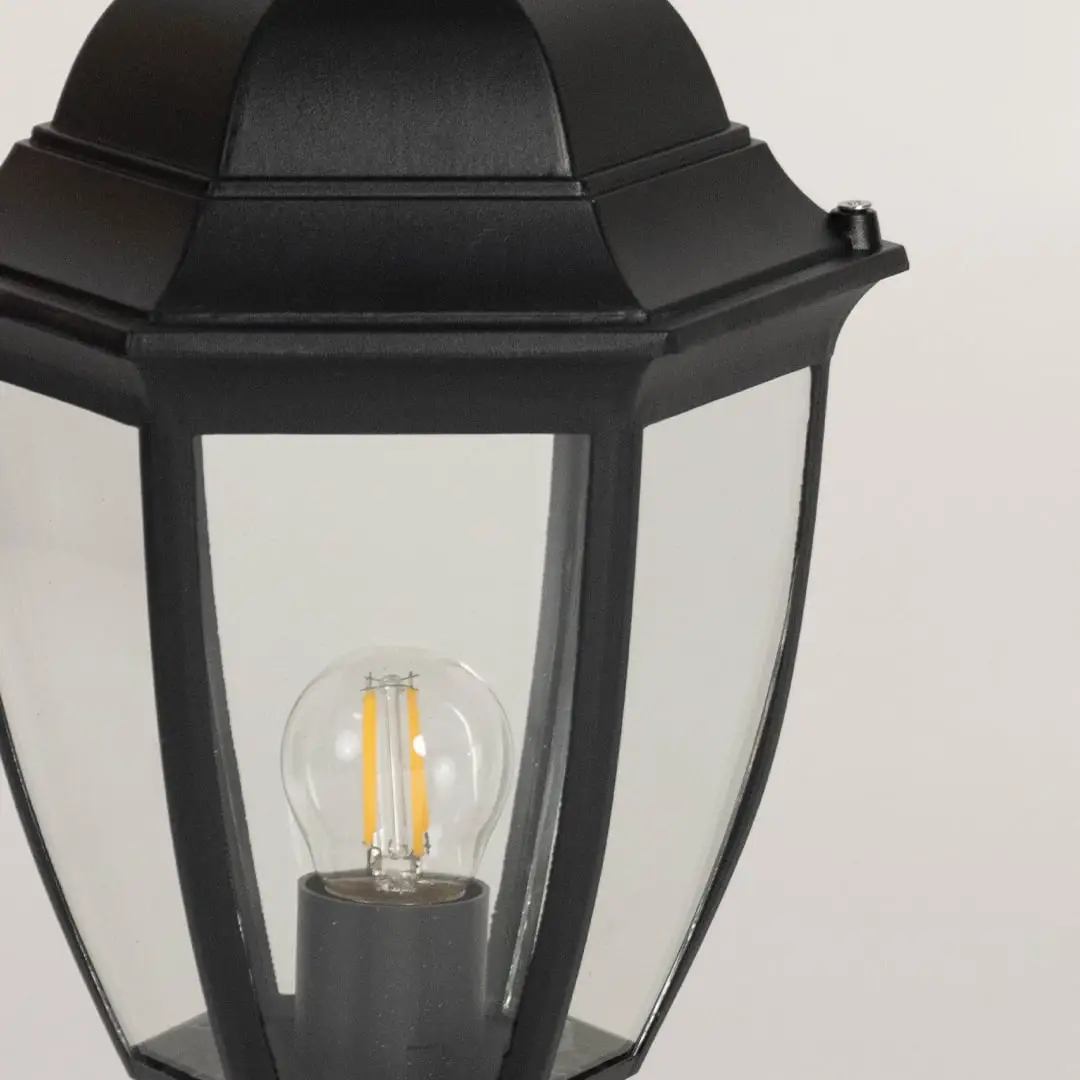 Closeup of outdoor black pillar lamp featuring transparent glass panels and LED bulb design with sleek modern finish.