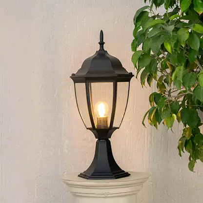 Elegant outdoor black pillar light glowing warmly with clear glass shade suitable for entrance patio and landscape use.