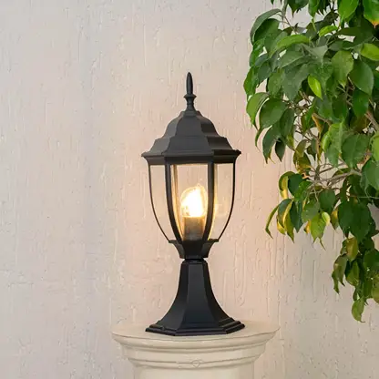 Outdoor black pillar light glowing warmly with LED bulb and clear glass shade suitable for patio garden and balcony use.