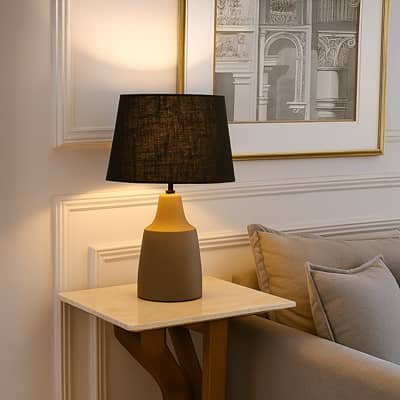 Modern table lamp with black fabric shade and smooth grey base adding warm ambient lighting that enhances stylish contemporary interior home decor settings.