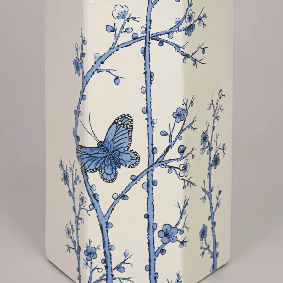 Closeup of cream ceramic vase showcasing detailed blue floral branches butterfly motif and smooth glazed finish.