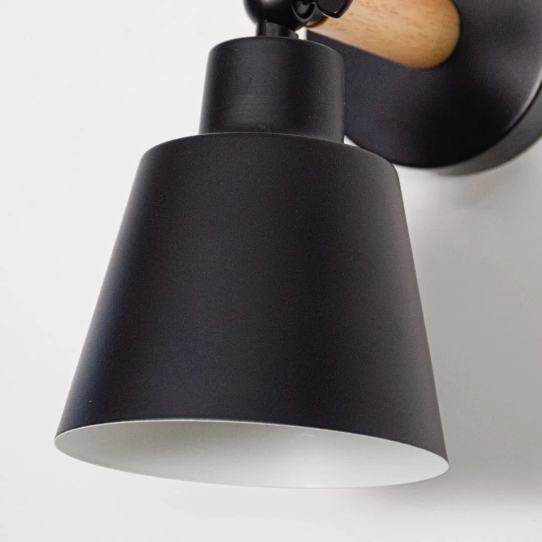 Black metal wall light closeup showing matte finish shade and curved arm detail designed for modern minimalist interior lighting.