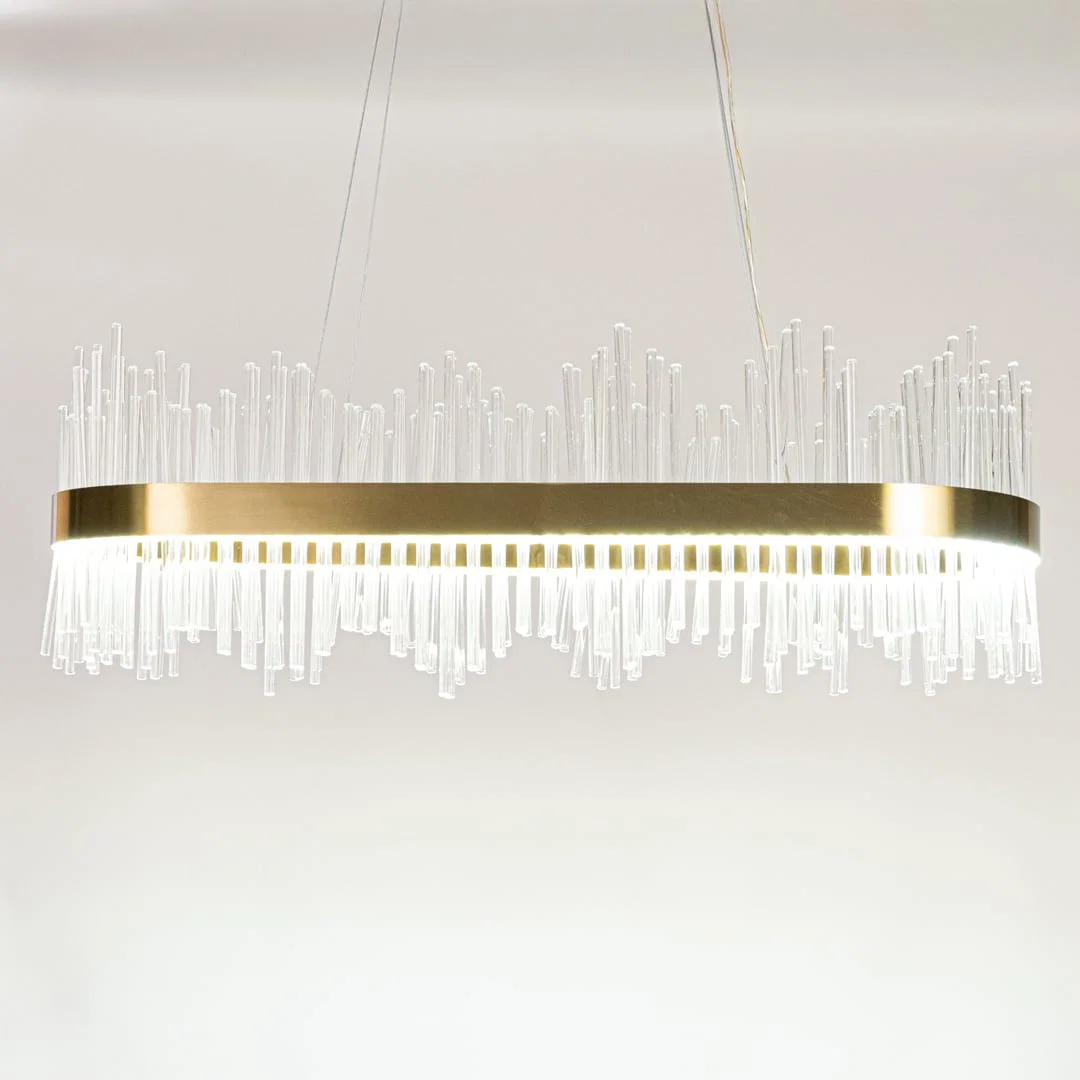 Gold metal chandelier with layered glass rods shown with lights on against a white background emphasizing its warm glowing upscale design.