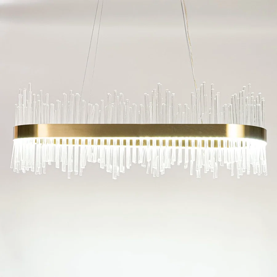 Gold metal chandelier with layered glass rods shown with lights on against a white background emphasizing its warm glowing upscale design.