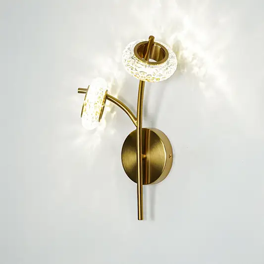Gold finish wall light with clear textured glass shade emitting bright light perfect for modern wall decor placement on clean background.