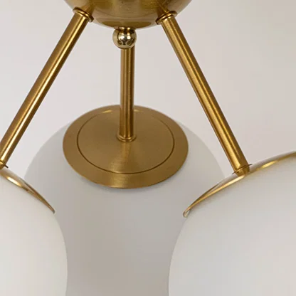 Closeup of gold ceiling light with three frosted glass globes on sleek frame for modern home lighting and ceiling decor.