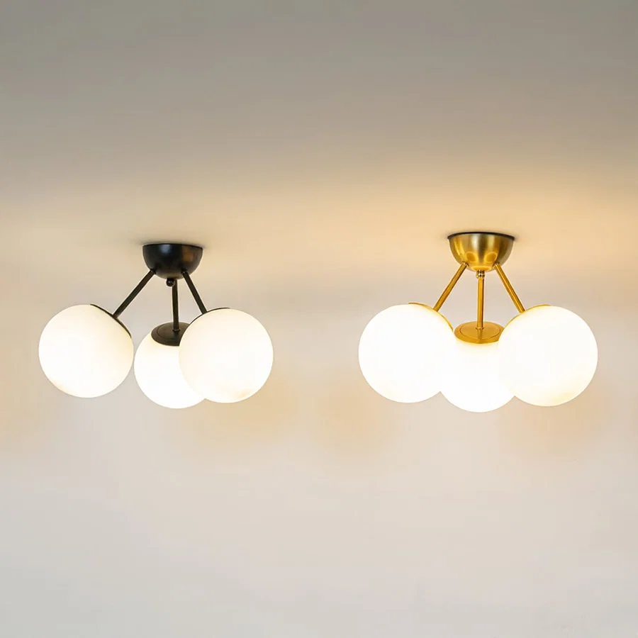 Black and gold ceiling lights with triple frosted glass globes glowing on white background for stylish home ceiling decor.