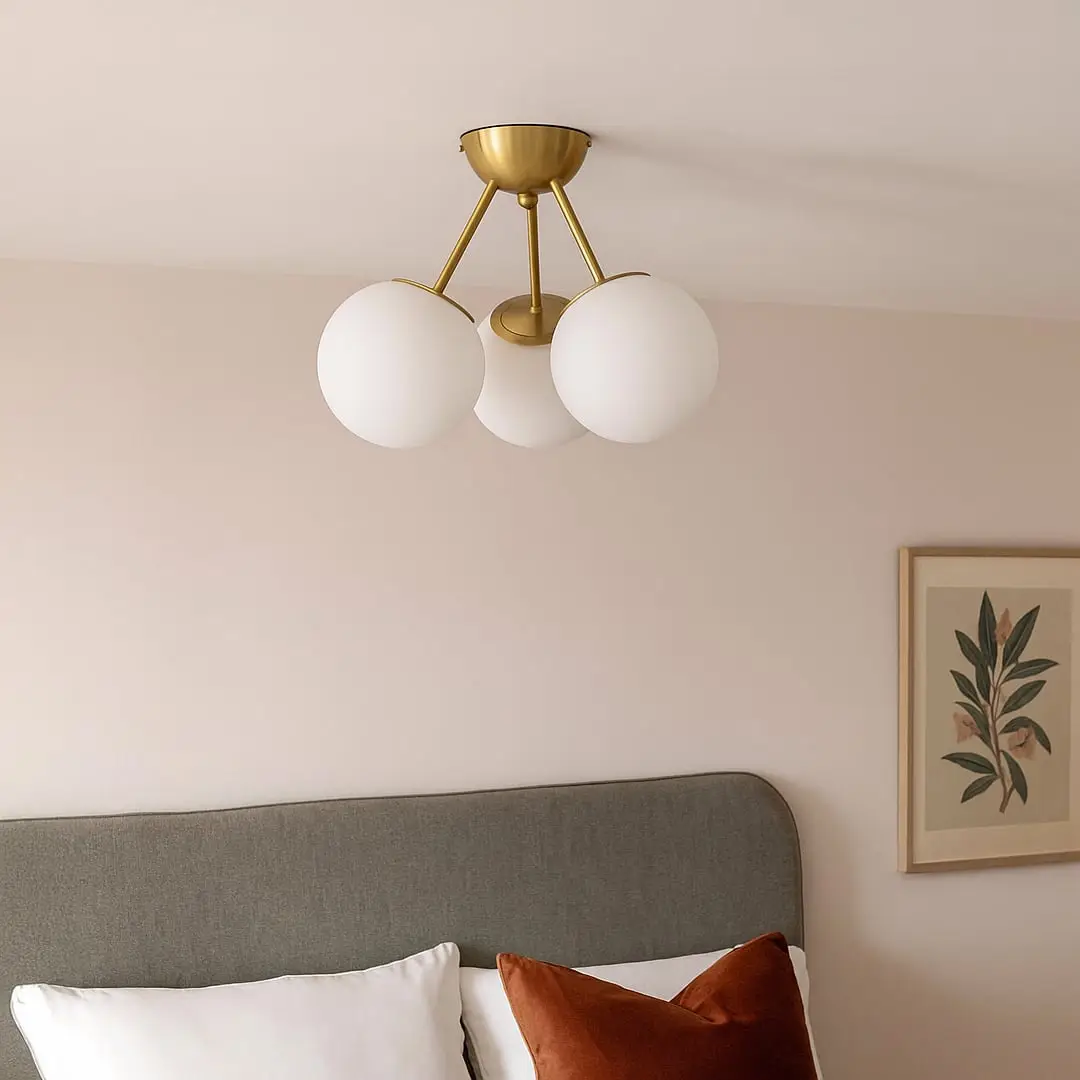 Modern gold ceiling light with three frosted glass globes glowing warmly above bed for elegant bedroom ceiling lighting.