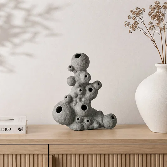 Grey abstract ceramic sculpture placed on wooden shelf with dried flowers for modern home decor styling.