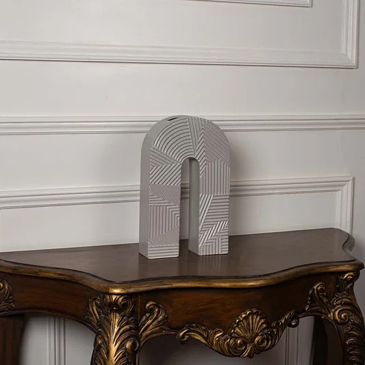 Modern arch shaped ceramic vase with geometric grey and white striped patterns displayed on a vintage wood console table.