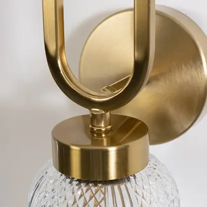 Closeup of luxury gold wall sconce with oval loop design and textured glass shade showing detailed craftsmanship and premium style.