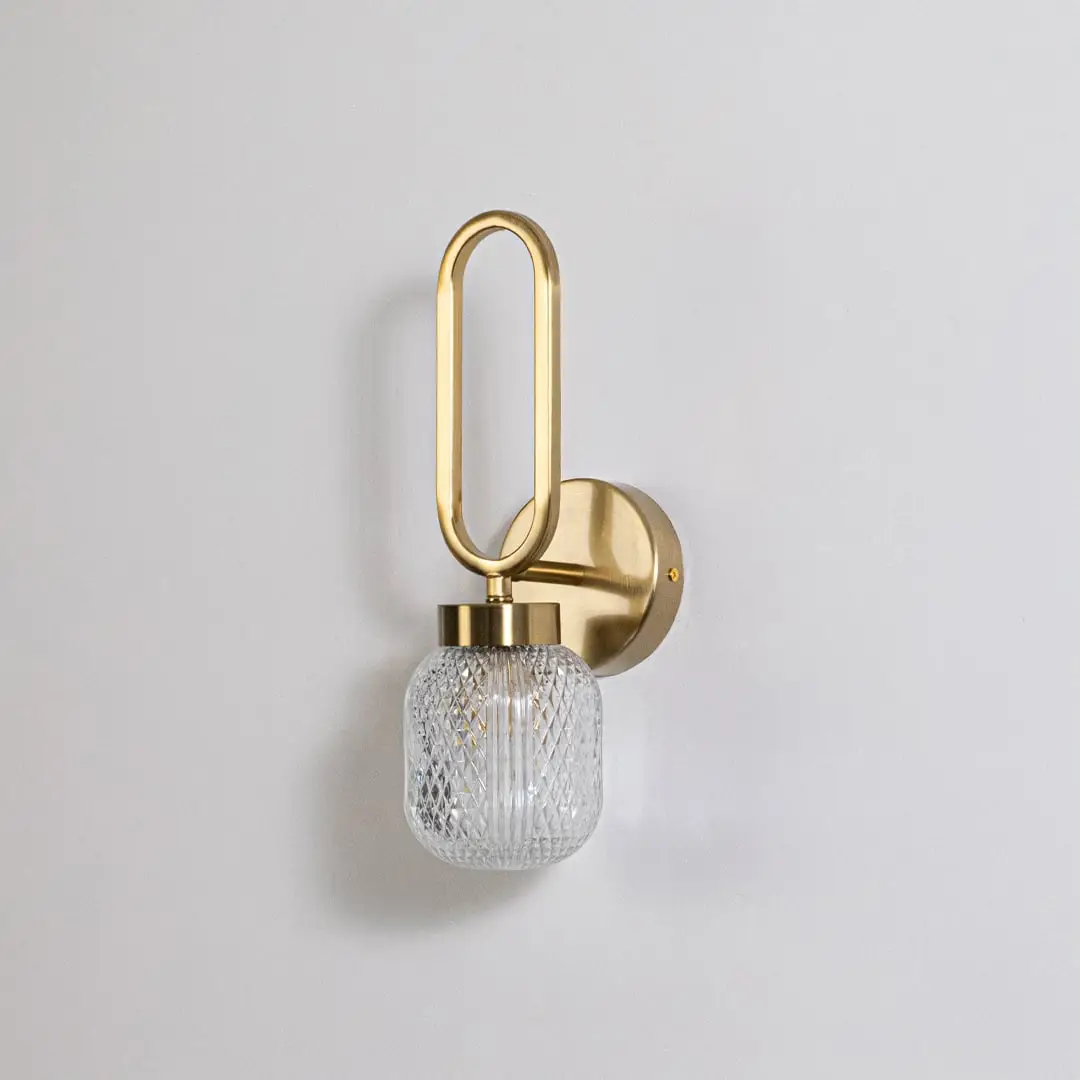 Minimalist gold wall sconce with loop frame and textured glass shade switched off displayed on plain white background for product use.