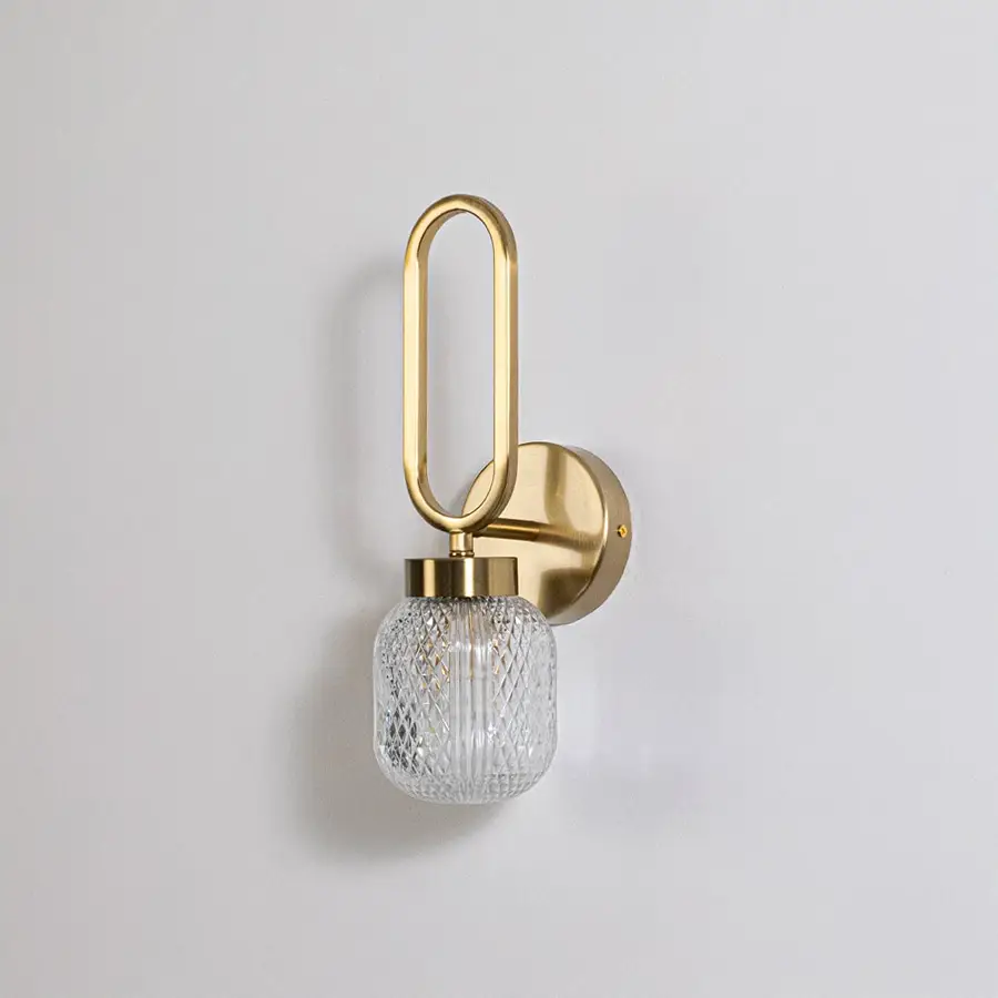 Minimalist gold wall sconce with loop frame and textured glass shade switched off displayed on plain white background for product use.