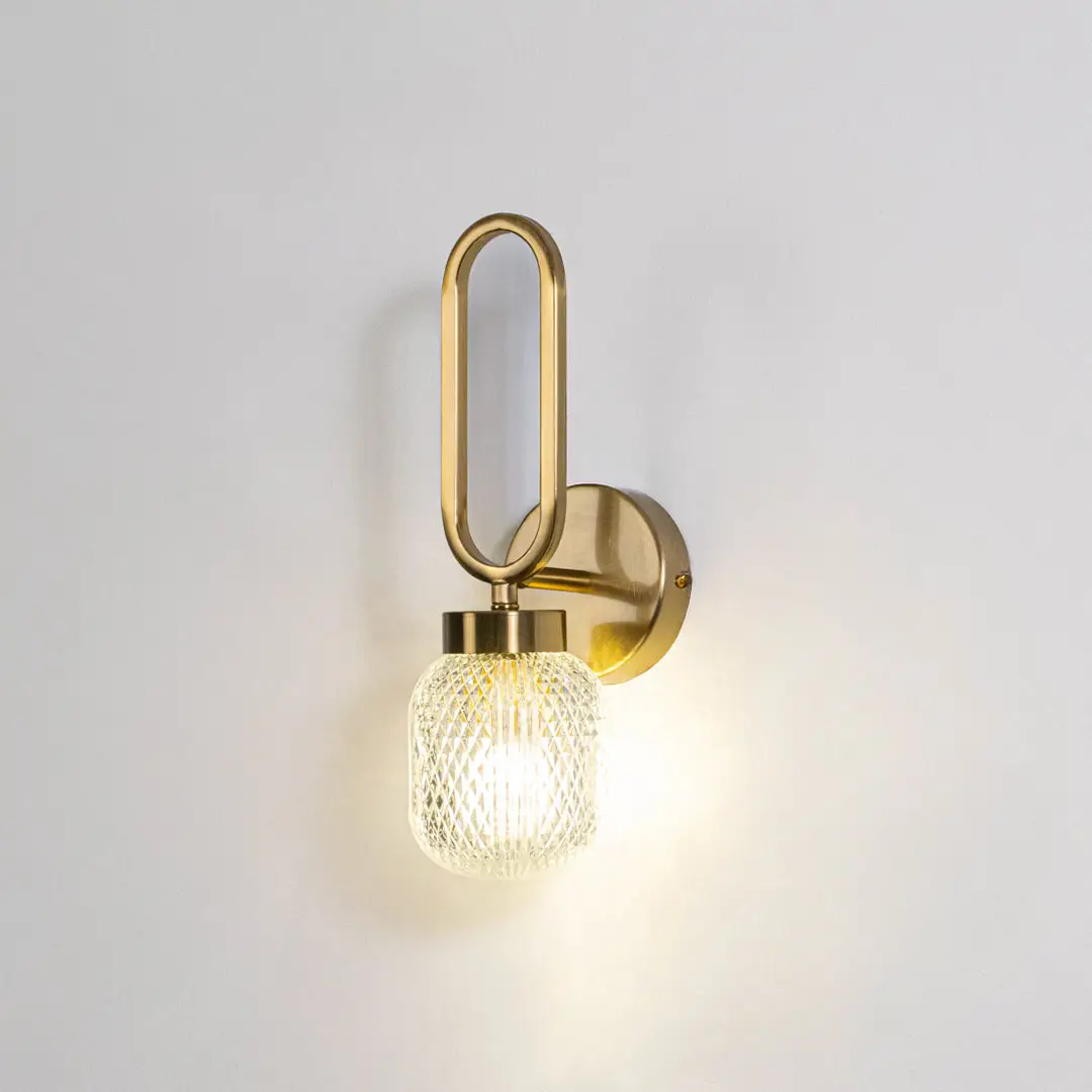 Modern wall light with gold metal frame and round glass bulb on neutral background minimal stylish lighting ideal for bedroom and living space decor.