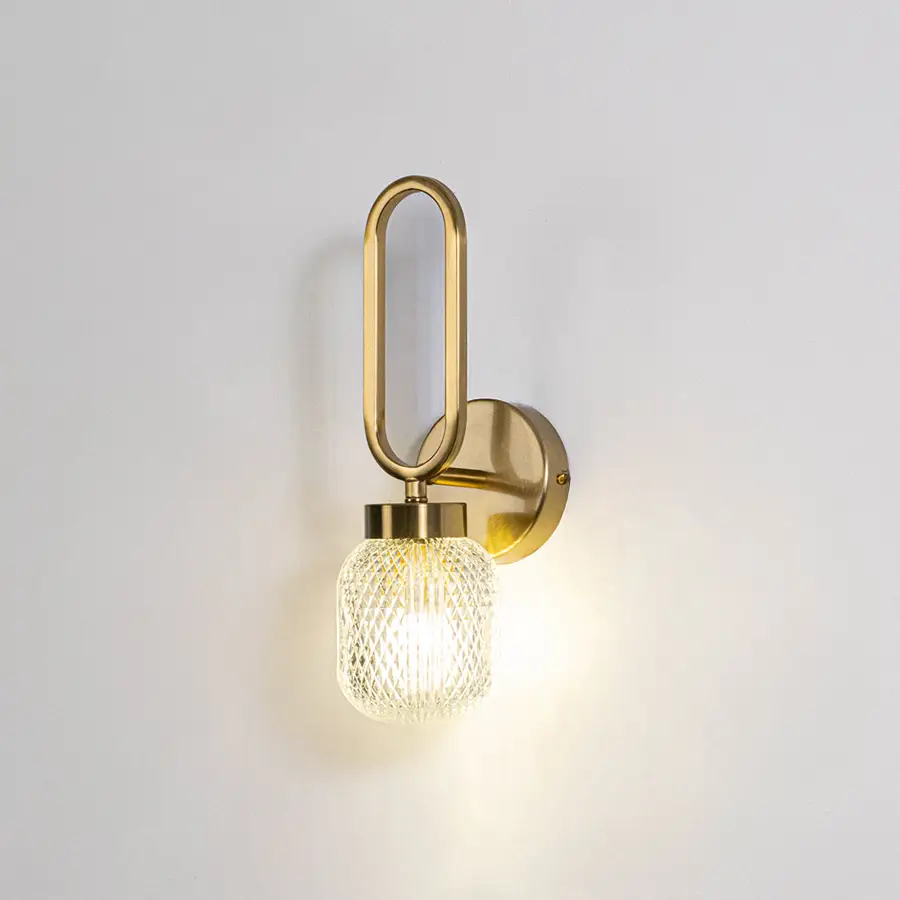 Modern wall light with gold metal frame and round glass bulb on neutral background minimal stylish lighting ideal for bedroom and living space decor.