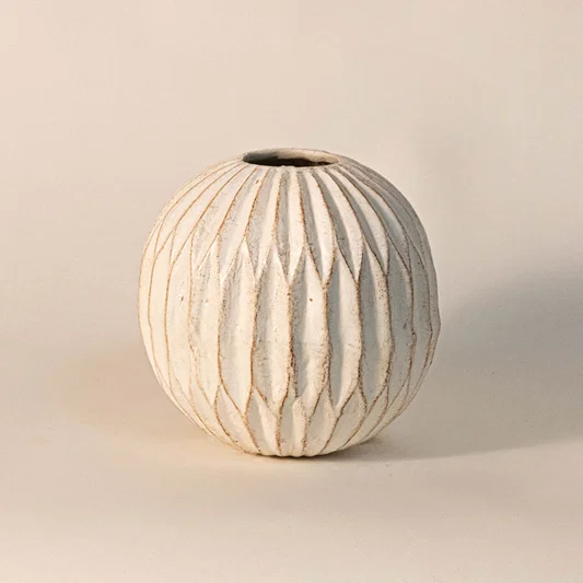 Modern ceramic vase in off white finish with carved ribbed design for table decor or shelf styling contemporary home placement white background.