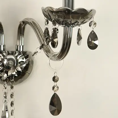 A close-up of a wall-mounted crystal chandelier with polished silver metal arms and faceted teardrop crystal drops in smoky gray and clear glass.