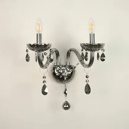 A two-light wall sconce with curved arms, a polished silver-toned metal body, and hanging faceted crystal prisms, shown against a plain off-white wall.