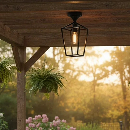 Black metal outdoor ceiling light with clear glass shade glowing warmly under a wooden pergola creating a cozy garden seating ambience at sunset.