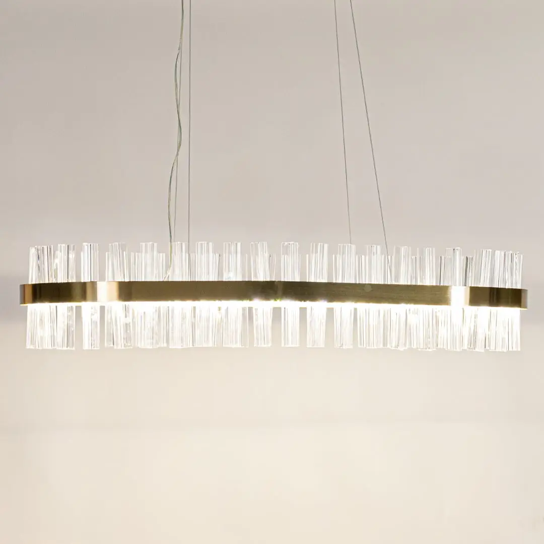 Gold metal chandelier with crystal rods shown with lights on creating a warm luxurious glow for modern interior spaces.
