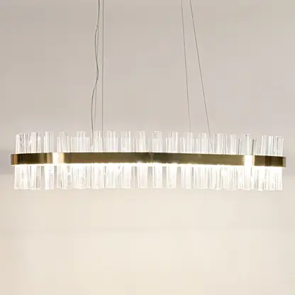 Gold metal chandelier with crystal rods shown with lights on creating a warm luxurious glow for modern interior spaces.