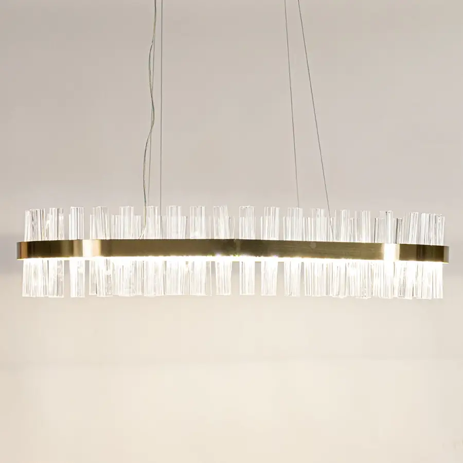 Gold metal chandelier with crystal rods shown with lights on creating a warm luxurious glow for modern interior spaces.