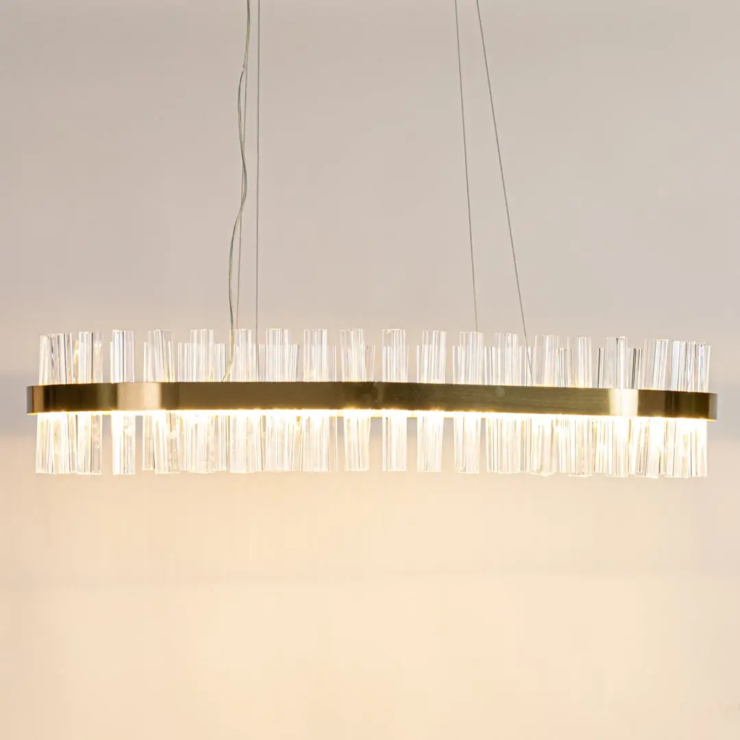 Gold metal chandelier with clear crystal rods displayed with lights on highlighting its sleek modern elongated frame.