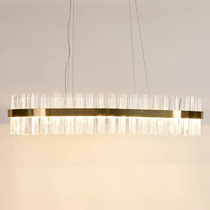 Gold metal chandelier with clear crystal rods displayed with lights on highlighting its sleek modern elongated frame.