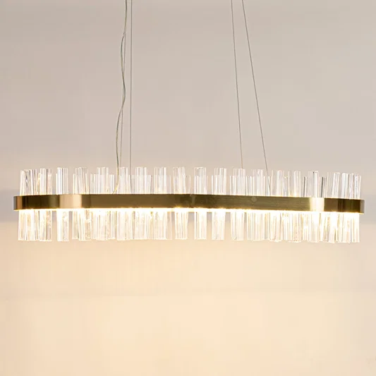 Gold metal chandelier with clear crystal rods displayed with lights on highlighting its sleek modern elongated frame.