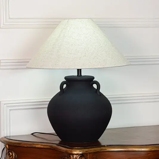 Black ceramic table lamp featuring textured matte finish rounded pot base and wide fabric shade displayed on white background.