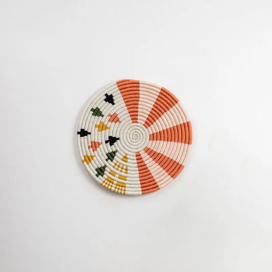 Round handcrafted seagrass wall basket with coral orange cream and black pattern on white background image.