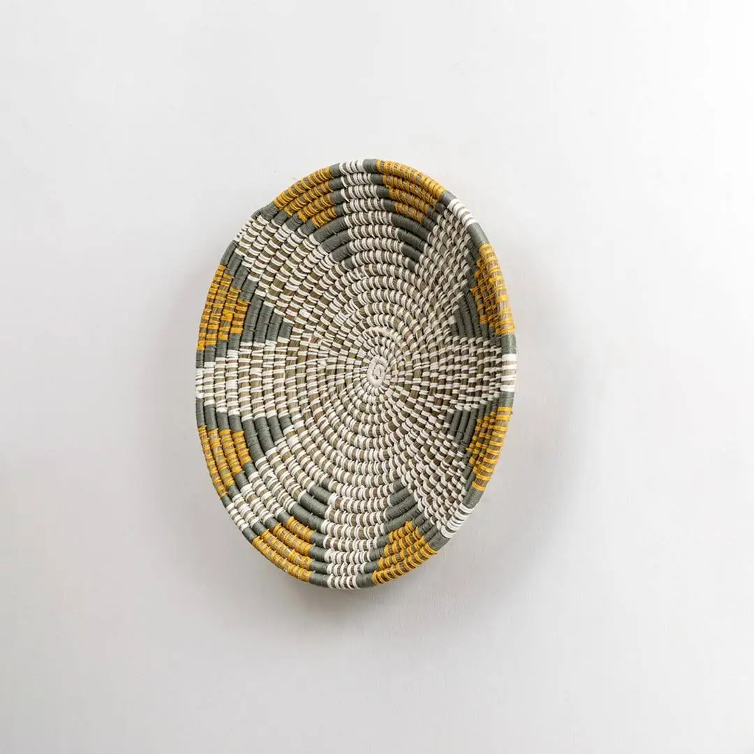 Round natural seagrass wall basket with white and mustard pattern for home décor on white background image.