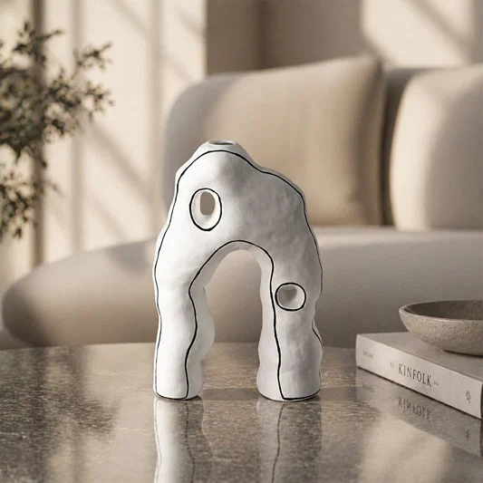 White abstract ceramic sculpture placed on marble table for elegant modern home decor styling.