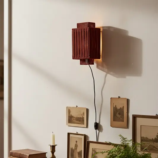 Wooden wall light with vertical slatted shade casting warm ambient glow on white wall styled with vintage frames plants and decor accents.